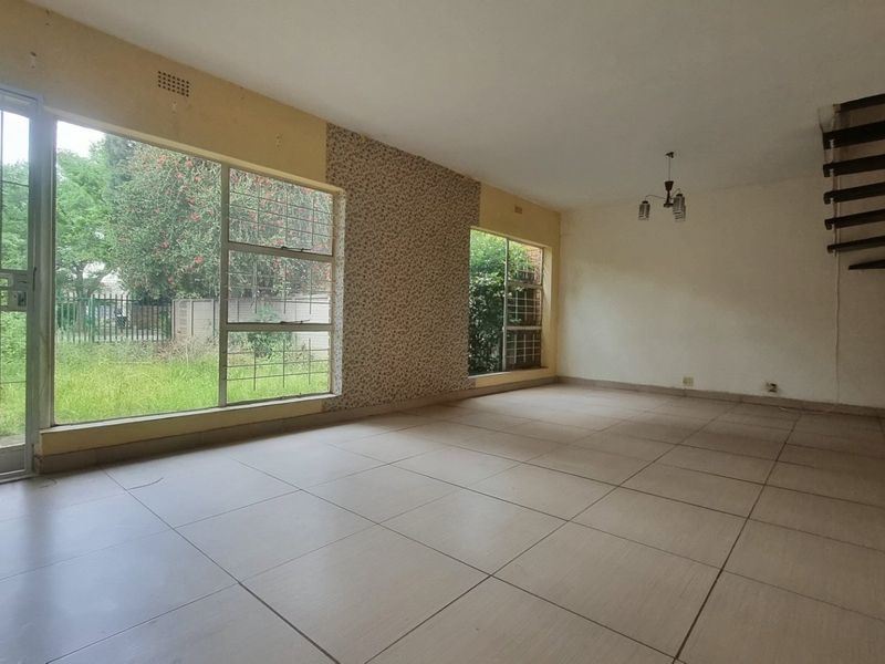 Spacious, empty living area featuring large windows, tiled flooring, and an open staircase, offering a blank canvas for renovation and modernization.