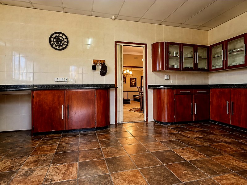 A functional kitchen featuring dark wood cabinetry, tiled splashbacks, and durable floor tiles, offering a practical layout with ample storage space.