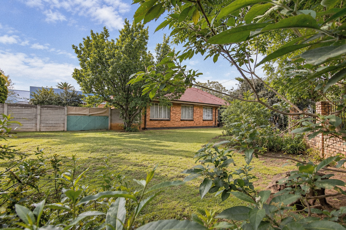 A view of the rear garden featuring a spacious lawn, established trees, and a brick house exterior with a tiled roof.