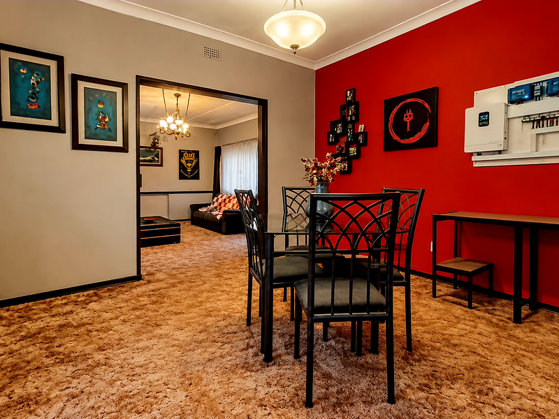 Dining room featuring a bold red accent wall, integrated solar power infrastructure, and carpeted flooring, with an open transition to the adjacent living area.