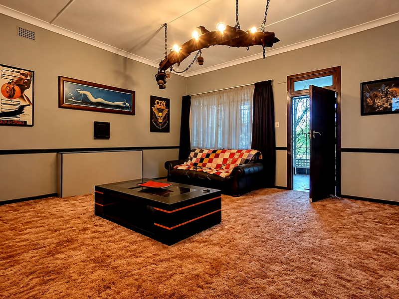 A living room featuring neutral wall tones, carpeted flooring, and a unique rustic chandelier, with direct access to an outdoor area.