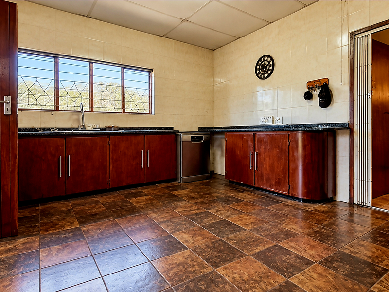 A spacious kitchen featuring dark wood cabinetry, granite countertops, tiled walls and flooring, and a large window with security bars.