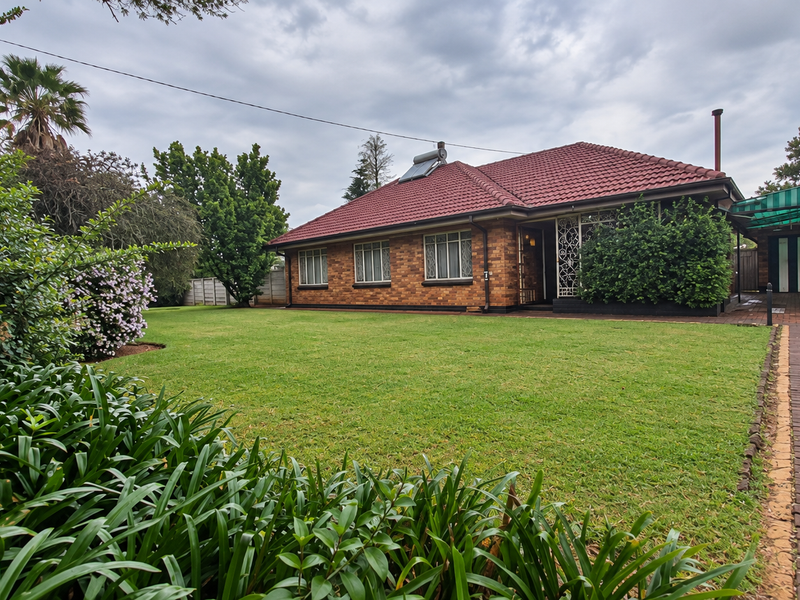 A well-maintained single-story brick house featuring a tiled roof, solar water heater, paved driveway, and a spacious front garden.