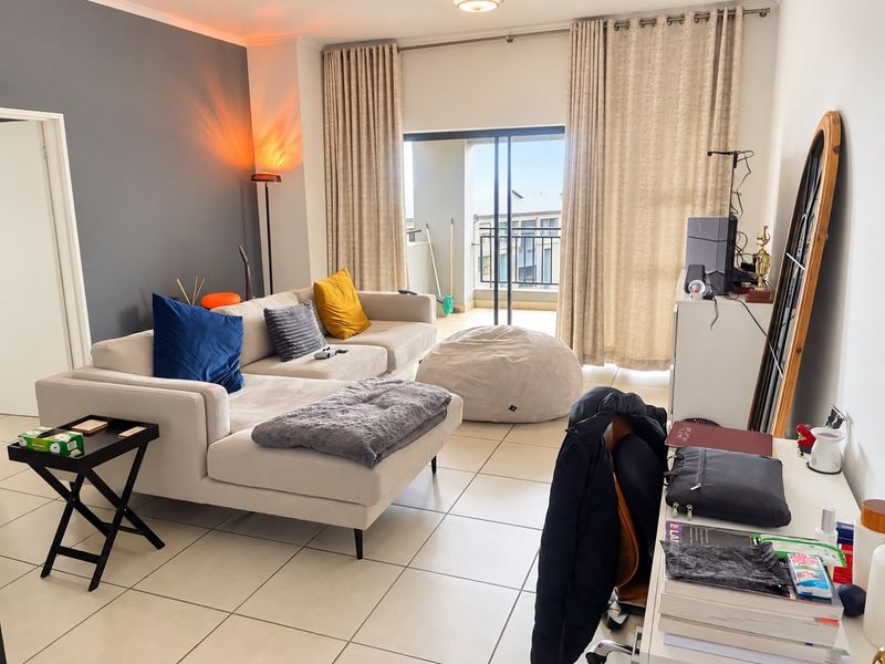 A bright living room featuring tiled flooring and a large sliding glass door providing access to a private balcony.