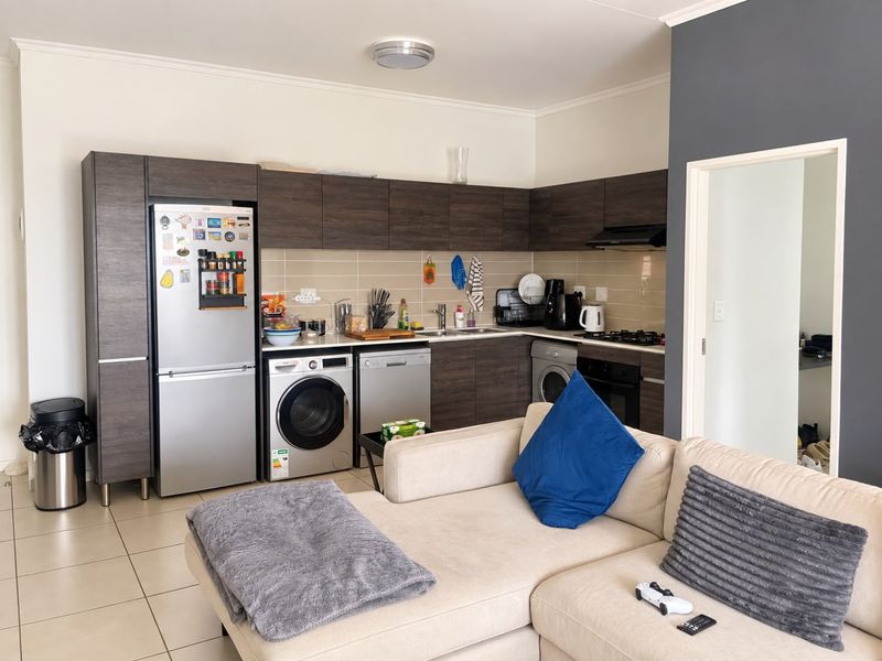 Open-plan kitchen featuring dark wood cabinetry, tiled backsplash, integrated appliances, and tiled flooring, seamlessly connected to the living area.