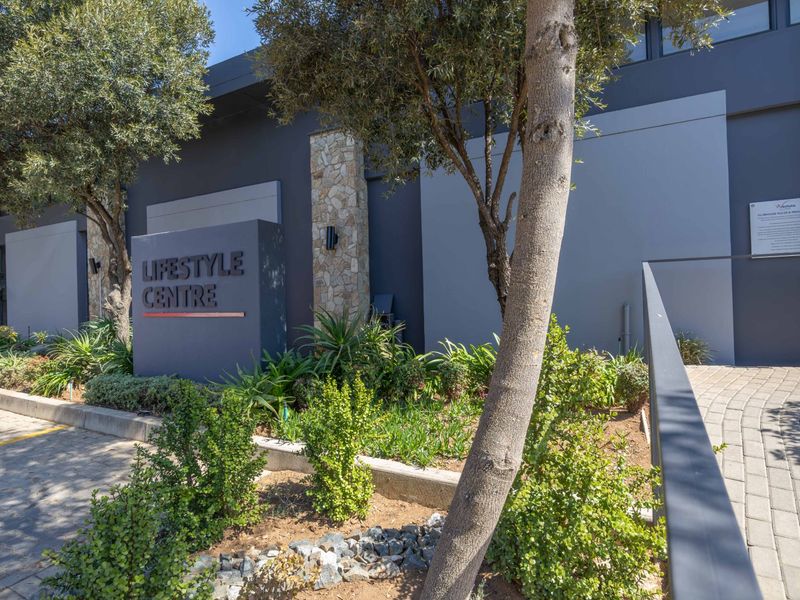 Exterior view of the apartment complex lifestyle centre, featuring modern dark grey facade, stone accents, and landscaped garden area.