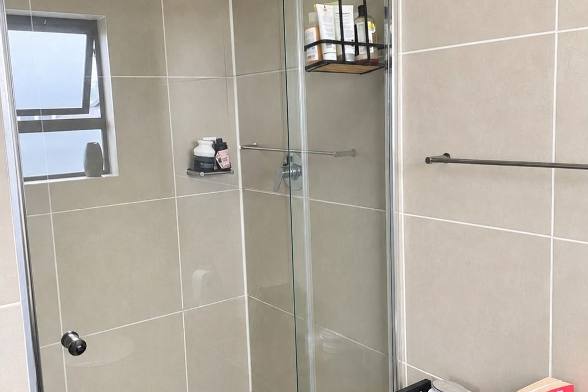 A modern bathroom shower area featuring neutral wall tiles, a glass enclosure, and a functional shower fixture.