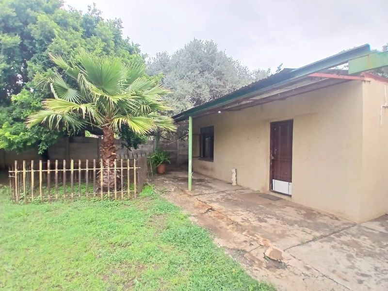 Rear exterior view of the property featuring a concrete patio area, metal roofing, and a garden space with perimeter fencing.