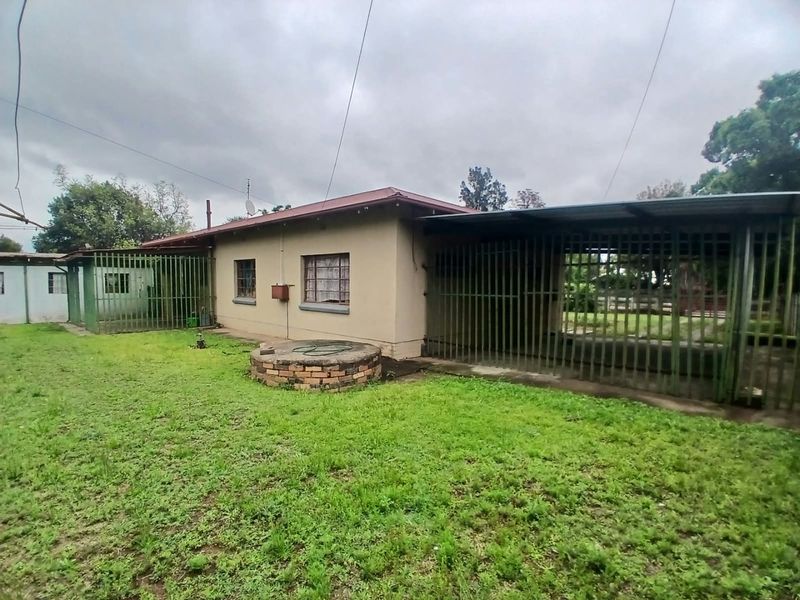 Rear view of the property featuring a lawn, brick well structure, and extensive metal security fencing with an attached carport area.