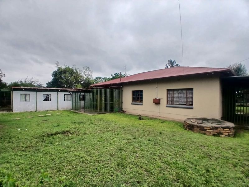 Rear view of the house featuring a metal roof, brick masonry, security bars on windows, and a brick well structure in the backyard.