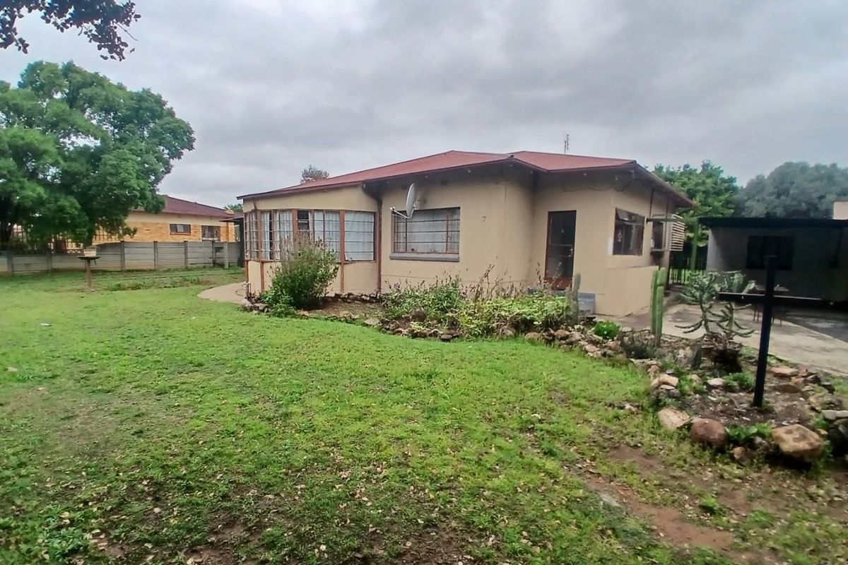 Rear view of a single-story house featuring a metal roof, steel-framed windows, and a spacious garden area with a concrete driveway.