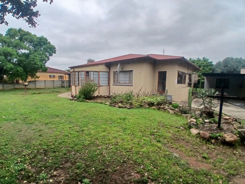 Rear view of a single-story house featuring a metal roof, steel-framed windows, and a spacious garden area with a concrete driveway.