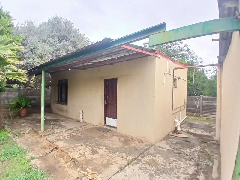 Rear exterior view of the property featuring a concrete patio area, corrugated metal roofing, and exposed exterior plumbing fixtures.