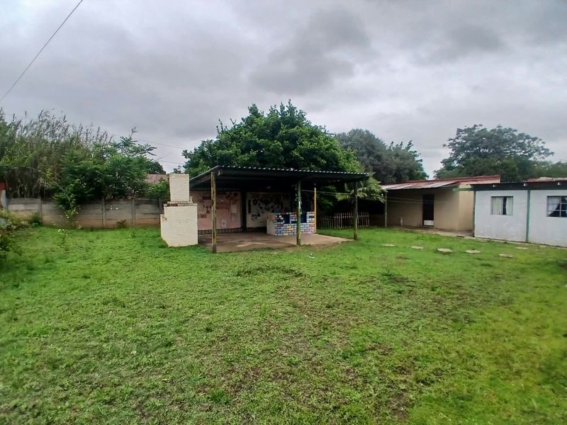 Spacious rear garden featuring a covered patio area with a built-in braai, offering potential for outdoor entertainment and landscaping improvements.