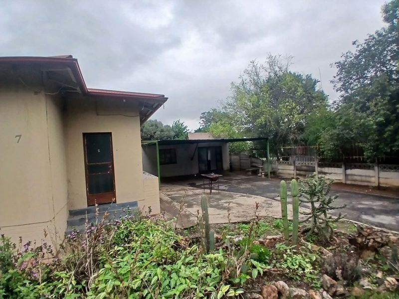 Rear view of the property featuring a concrete patio area, covered outdoor space, and a precast boundary wall in a garden setting.