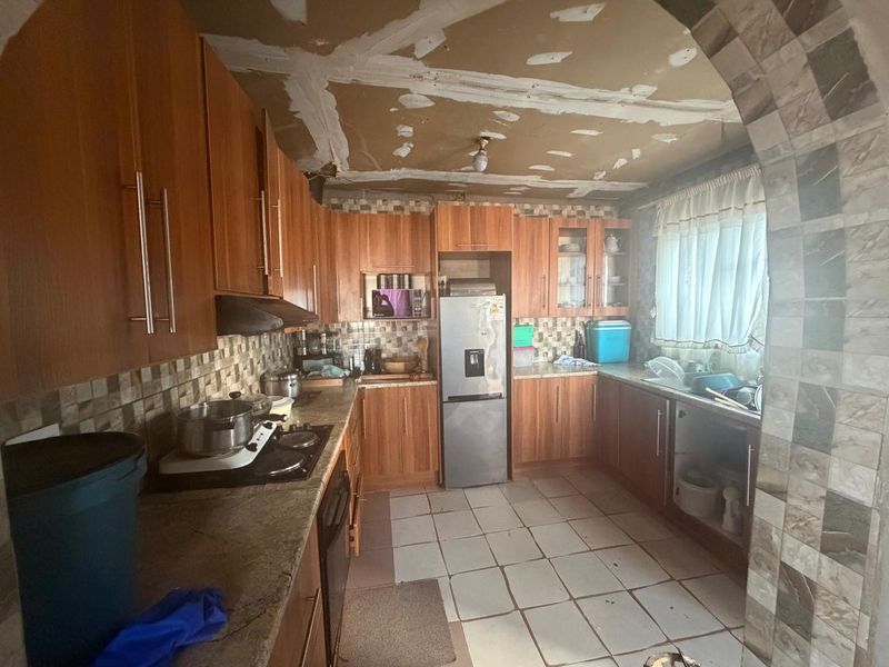 A kitchen featuring wood-look cabinetry and tiled surfaces, currently requiring ceiling repairs and general maintenance to restore its functionality and aesthetic appeal.