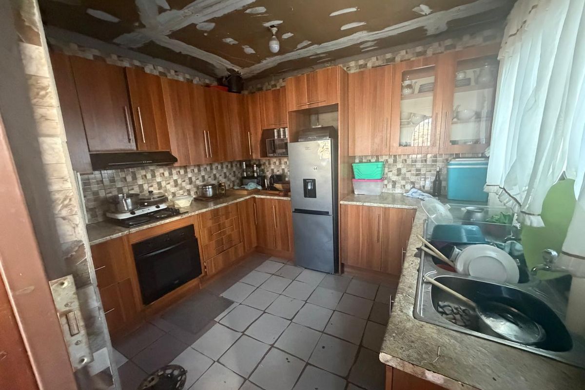 A dated kitchen featuring wooden cabinetry, laminate countertops, and a tiled backsplash, currently requiring ceiling and wall finishing to complete the space.