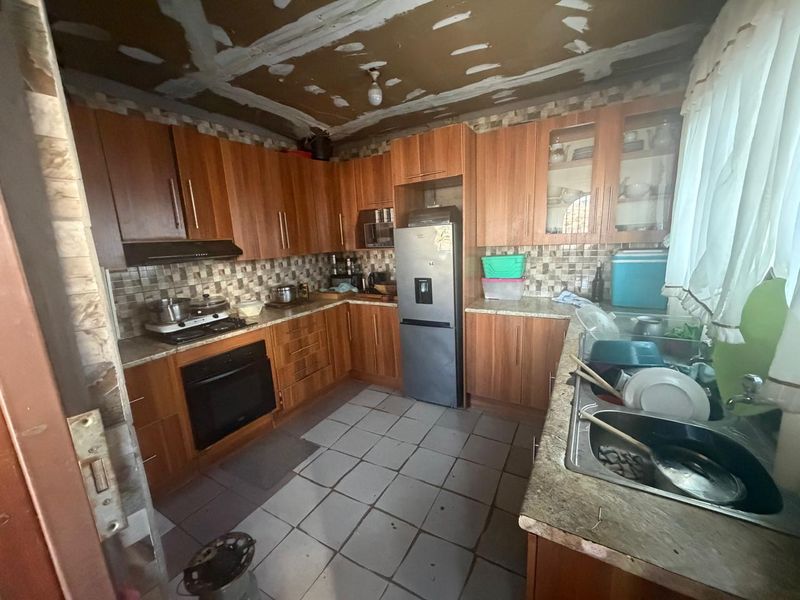 A dated kitchen featuring wooden cabinetry, laminate countertops, and a tiled backsplash, currently requiring ceiling and wall finishing to complete the space.
