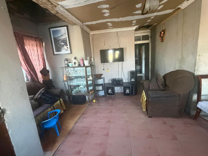 A living room space featuring tiled flooring and coving, currently requiring significant ceiling and wall repairs to improve the overall condition.