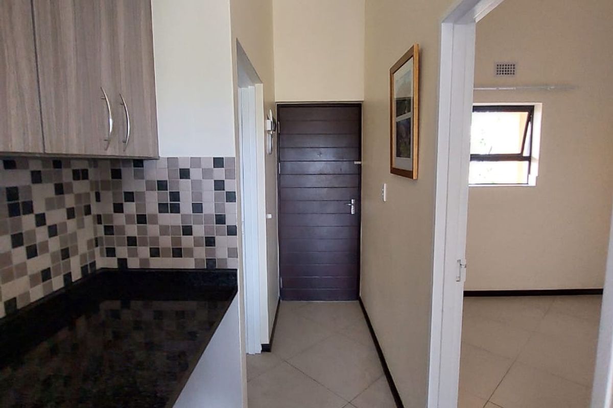 A clean, functional kitchen area featuring granite countertops, modern cabinetry, and neutral tiled flooring, leading into an adjacent room.