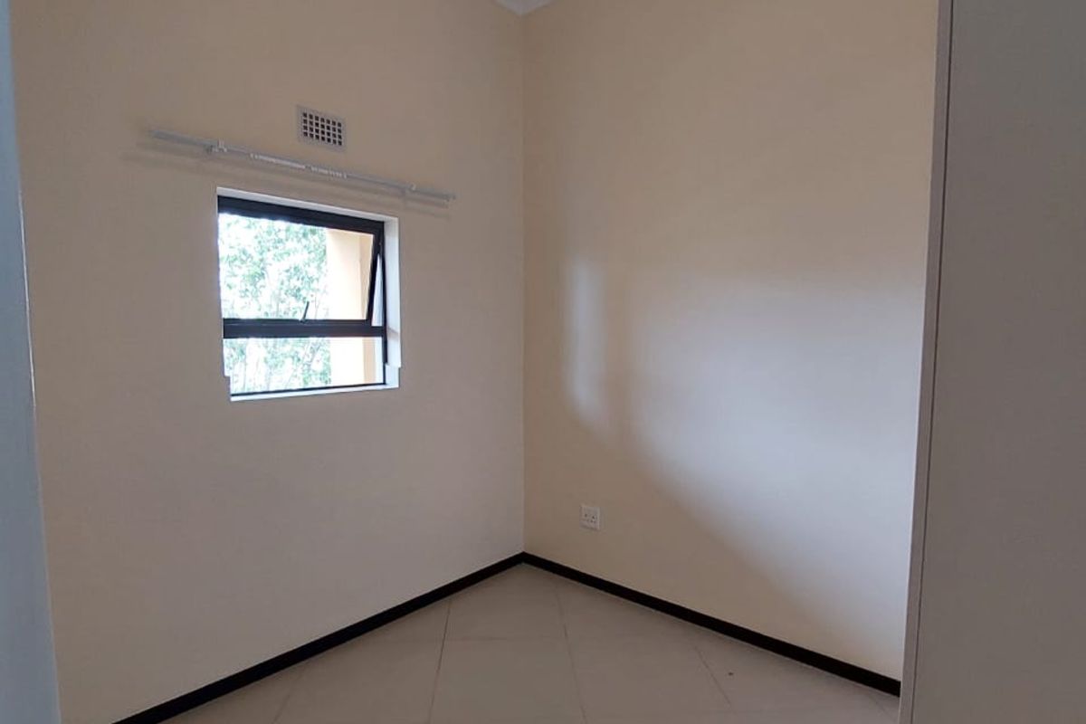 A clean, empty bedroom featuring neutral tiled flooring, a top-hung window, and a simple ceiling light fixture.