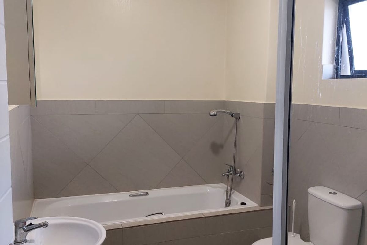 A clean, functional bathroom featuring a pedestal basin, bathtub with shower mixer, and a toilet, finished with neutral wall and floor tiling.