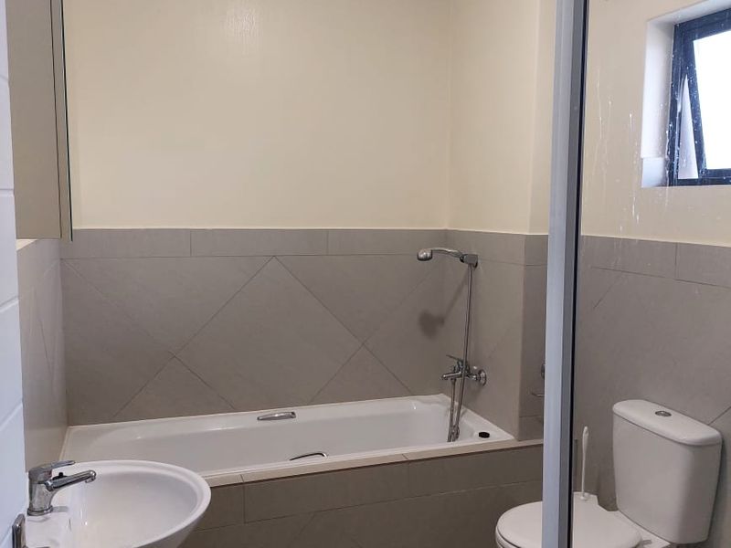 A clean, functional bathroom featuring a pedestal basin, bathtub with shower mixer, and a toilet, finished with neutral wall and floor tiling.