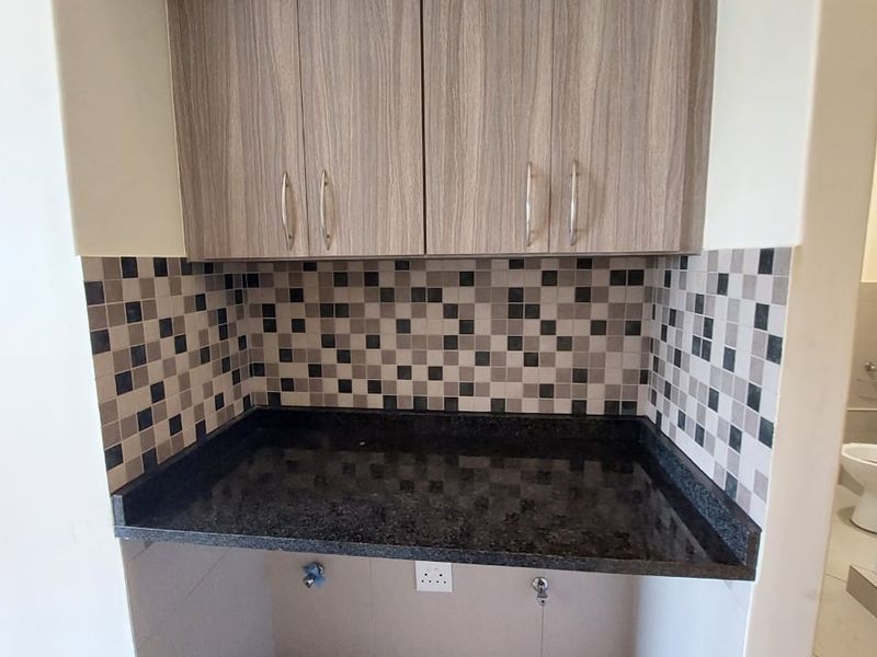 A compact laundry nook featuring built-in cabinetry, a durable granite countertop, and a decorative mosaic tile backsplash with dedicated plumbing and electrical connections.