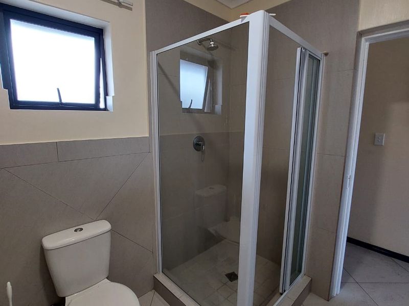 A clean, functional bathroom featuring a glass shower enclosure, a standard toilet, neutral wall tiling, and tiled flooring.