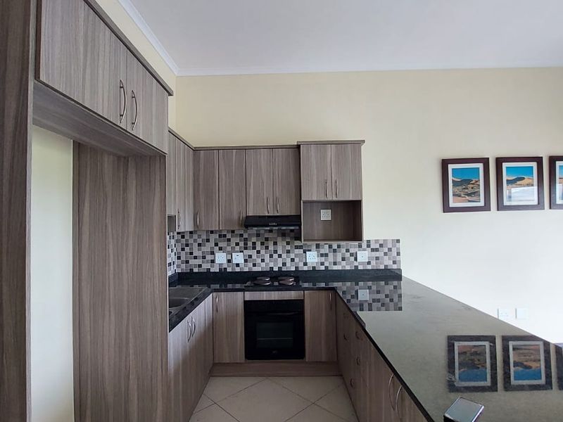 A functional kitchen featuring wood-finish cabinetry, granite countertops, a mosaic backsplash, and built-in appliances, offering a clean and practical layout.