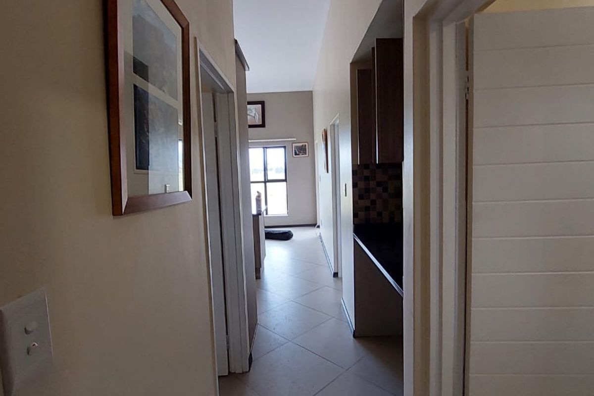 A view down a tiled hallway leading towards an open-plan living area, with a glimpse of the kitchen cabinetry and countertop to the side.
