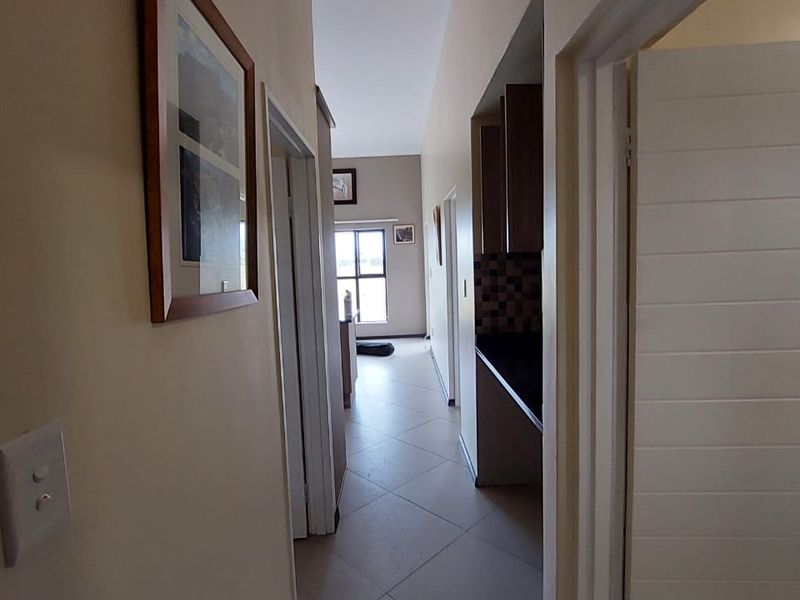 A view down a tiled hallway leading towards an open-plan living area, with a glimpse of the kitchen cabinetry and countertop to the side.