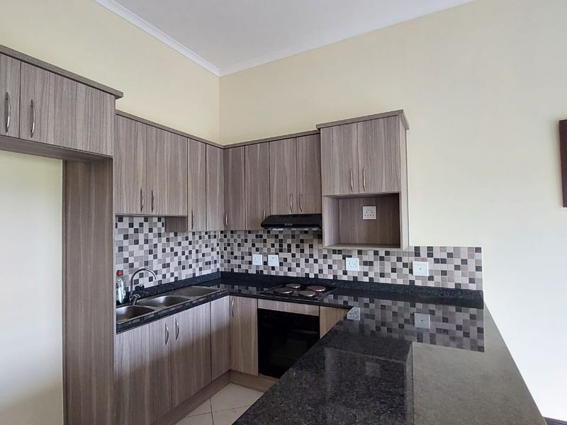 Modern kitchen featuring laminate cabinetry, granite countertops, a breakfast bar, and a mosaic tile backsplash, offering a functional and clean cooking space.
