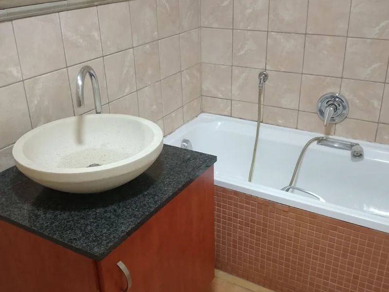 A functional bathroom featuring a vessel sink on a granite vanity, a bathtub with a handheld shower mixer, and neutral wall and floor tiling.