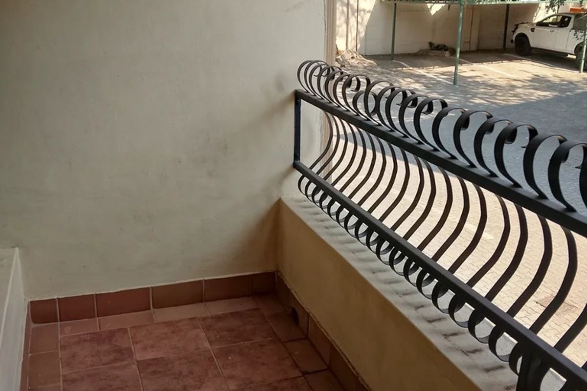 A compact balcony featuring tiled flooring and a decorative wrought iron balustrade, overlooking the parking area.