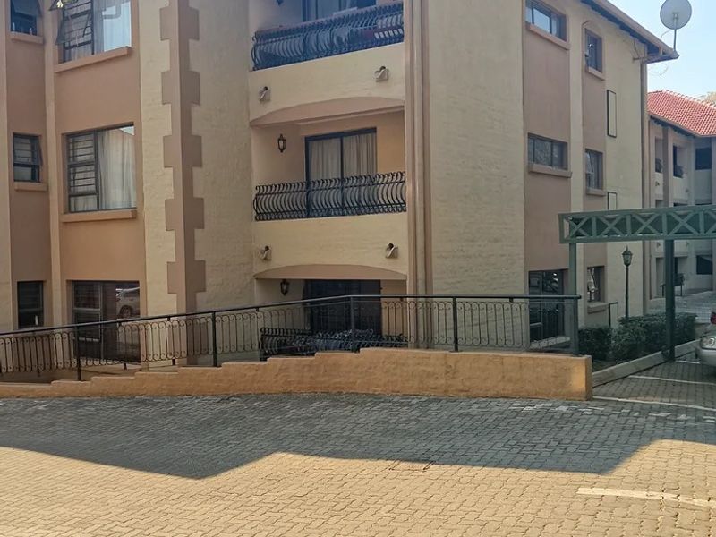 Exterior view of a multi-story residential building featuring paved driveway access, covered balconies with wrought iron railings, and a metal carport structure.