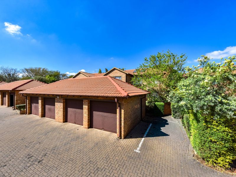 A row of brick-built garages with tiled roofs and roller shutter doors, situated in a paved complex driveway area.