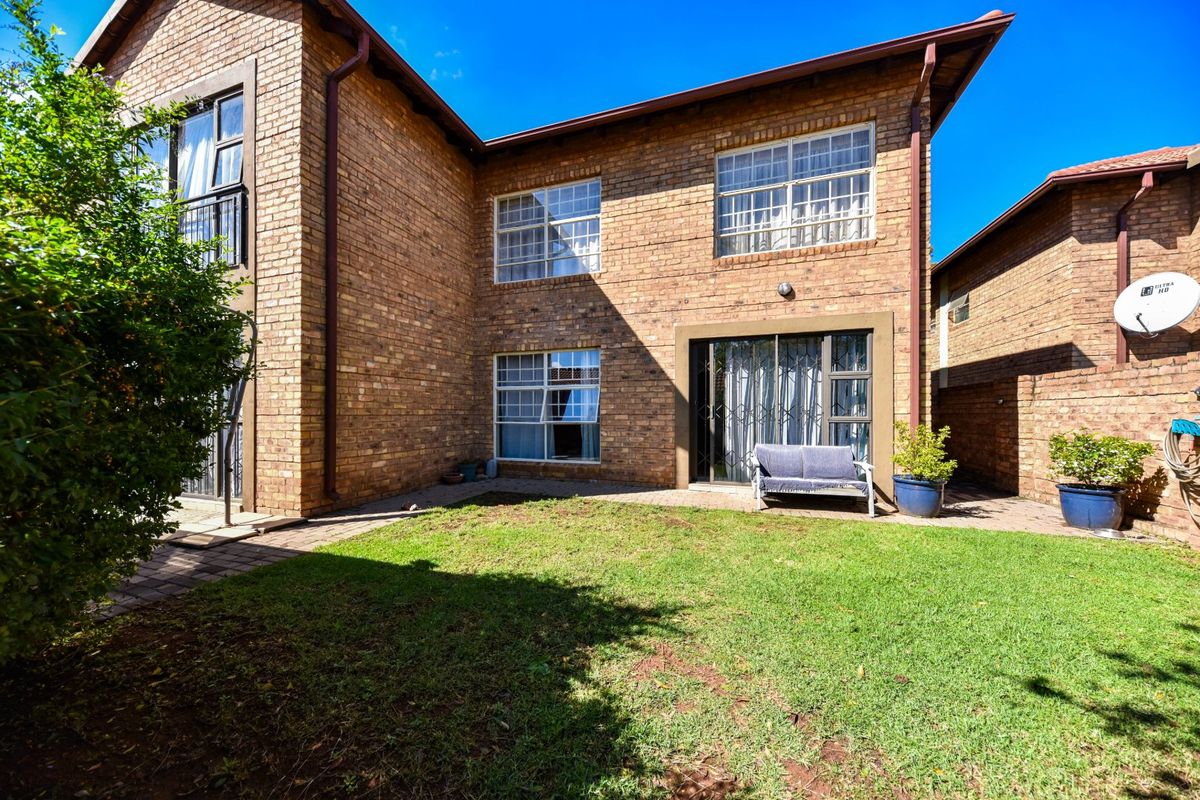 Rear view of a face brick townhouse featuring a paved patio area, small lawn, and sliding door access to the interior.