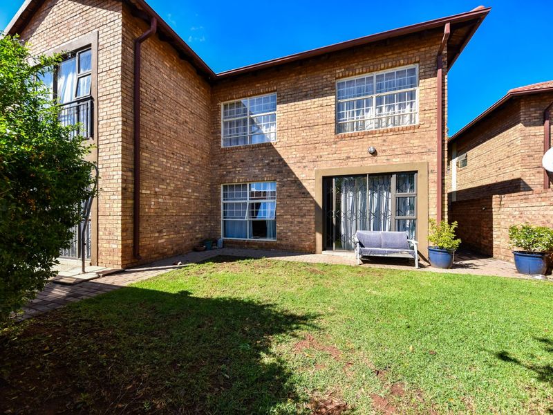 Rear view of a face brick townhouse featuring a paved patio area, small lawn, and sliding door access to the interior.