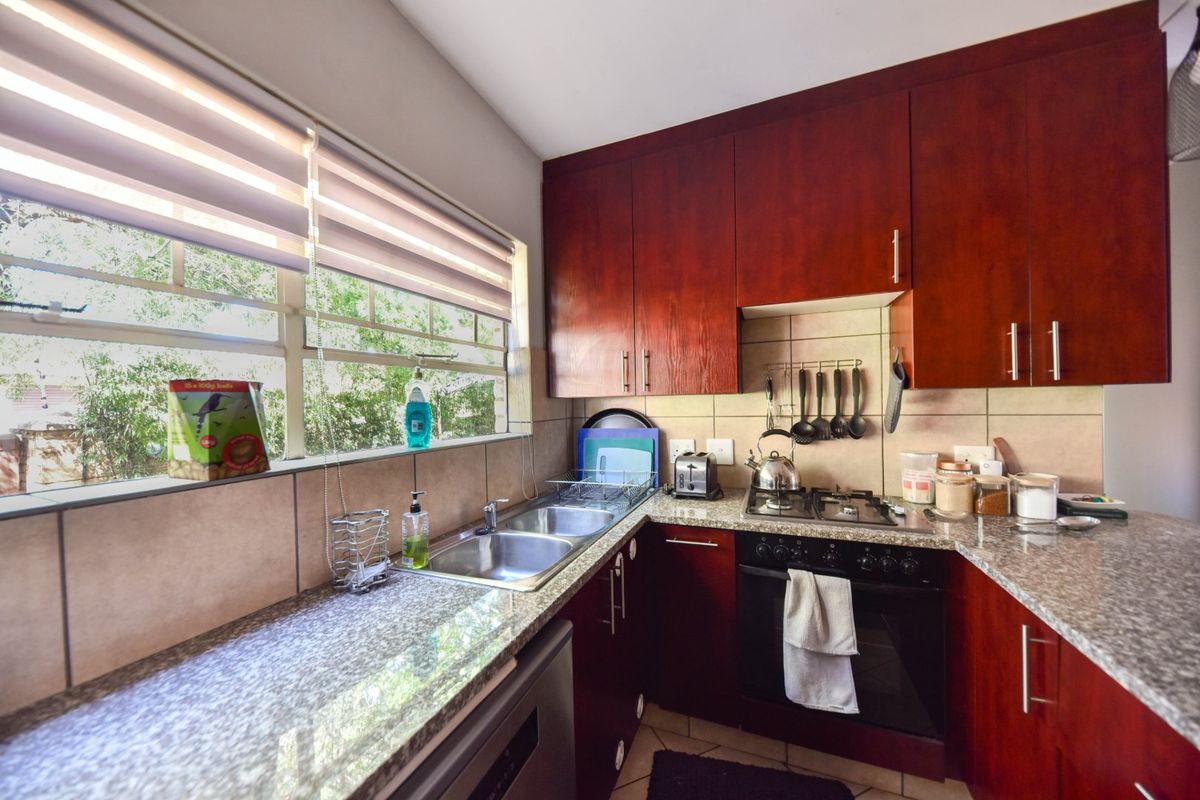 A functional kitchen featuring dark wood cabinetry, granite countertops, a built-in oven with gas hob, and a double basin sink under a window.