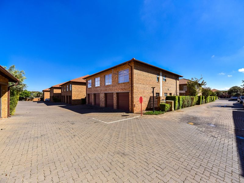 Exterior view of a townhouse complex featuring brick facades, tiled roofs, and a paved driveway with multiple garage access points.
