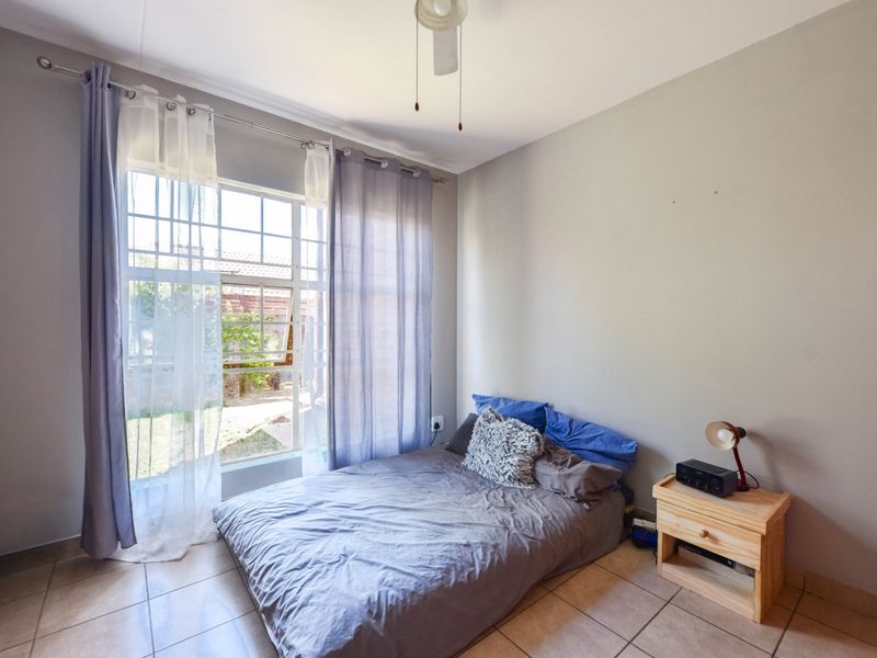 A bedroom featuring tiled flooring, a ceiling fan, and a large window providing natural light and garden views.