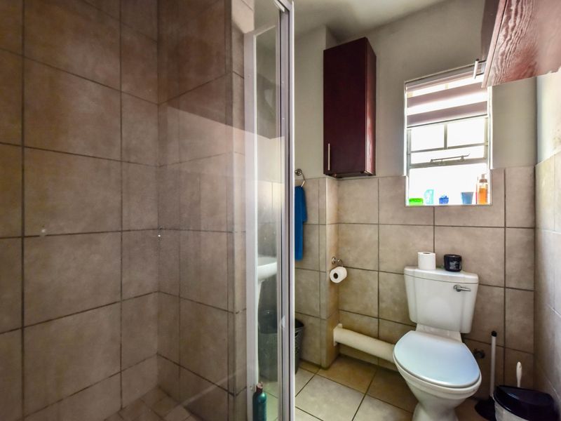 A functional bathroom featuring a shower enclosure, tiled walls and flooring, a standard toilet, and a wall-mounted storage cabinet.
