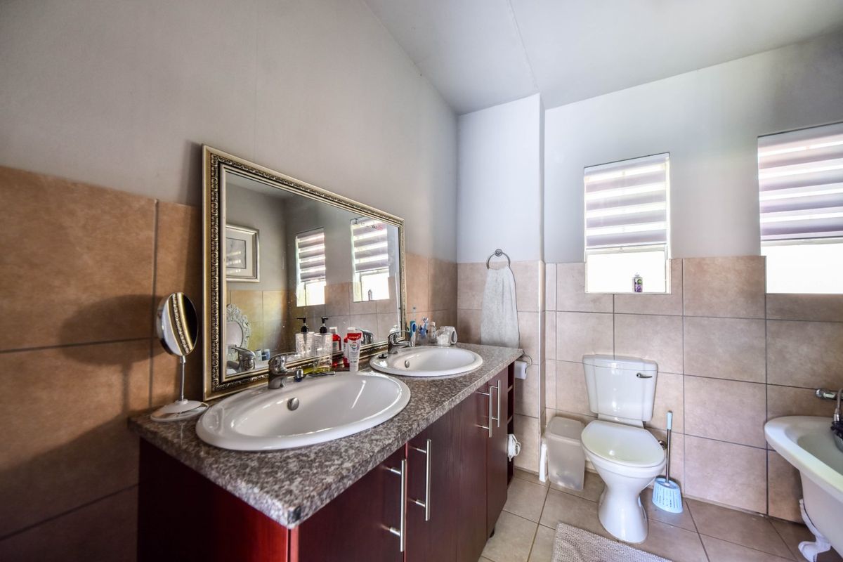 A functional bathroom featuring a double vanity with granite countertops, dual sinks, a toilet, and neutral ceramic wall and floor tiling.