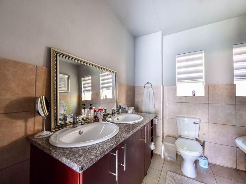 A functional bathroom featuring a double vanity with granite countertops, dual sinks, a toilet, and neutral ceramic wall and floor tiling.