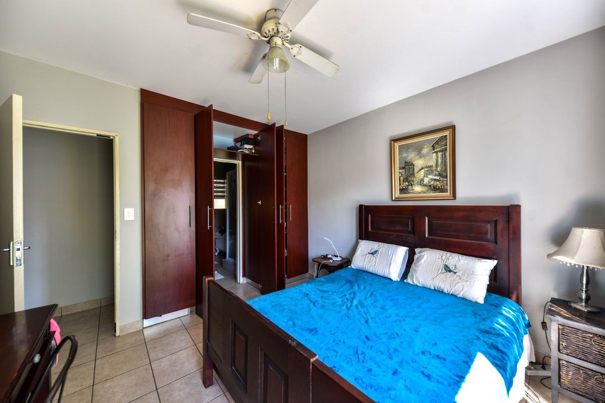 A bedroom featuring tiled flooring, a ceiling fan, and built-in wooden cupboards with an adjacent doorway.