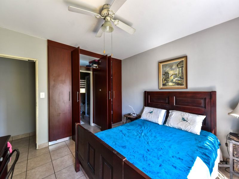 A bedroom featuring tiled flooring, a ceiling fan, and built-in wooden cupboards with an adjacent doorway.
