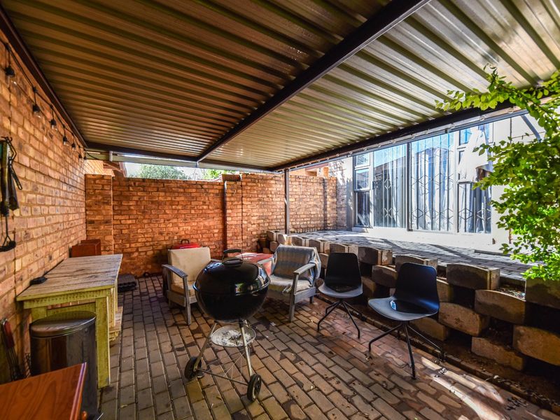 A covered outdoor patio area featuring exposed brick walls, a corrugated metal roof, and paved flooring, suitable for outdoor entertaining.