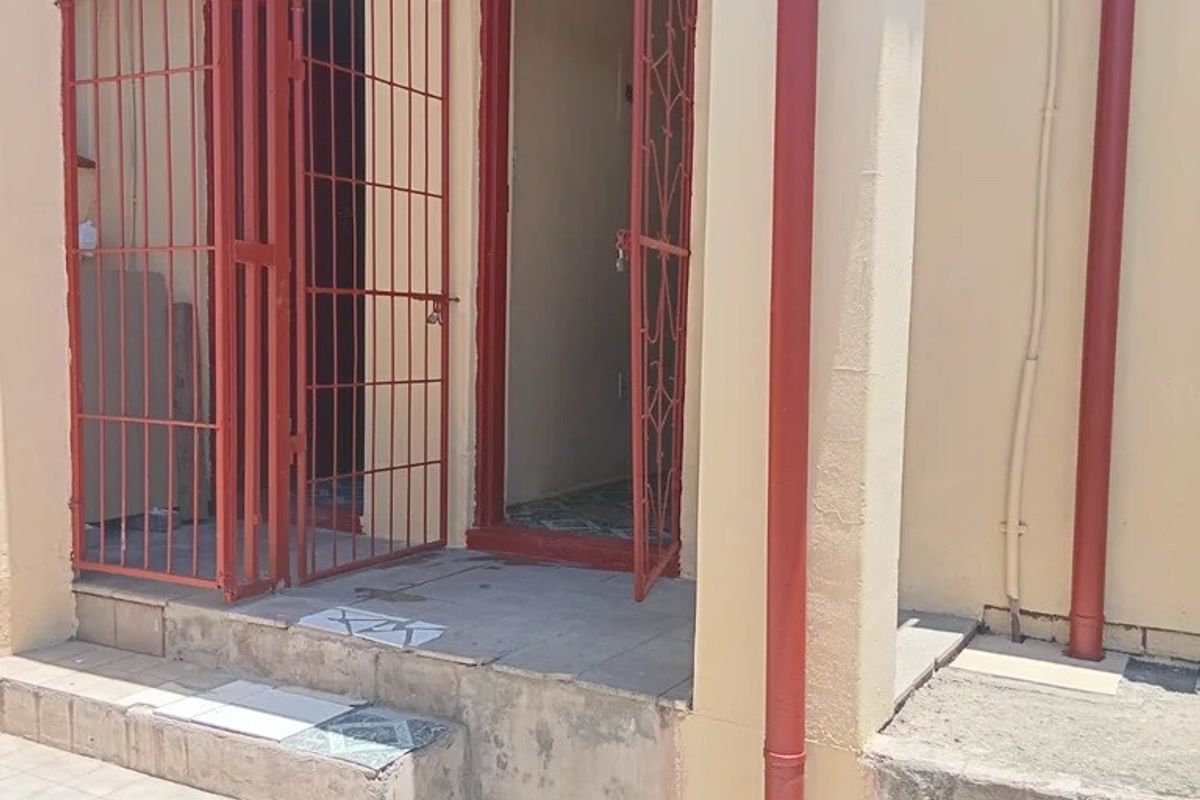 Rear exterior entrance featuring concrete steps, security gates, and exposed downpipes, showing signs of wear and weathering.