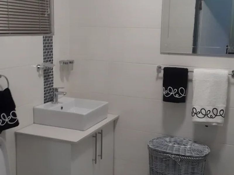 A clean, modern bathroom featuring a white vanity with a vessel sink, wall-mounted mirror, and neutral tiled finishes with a decorative mosaic accent.